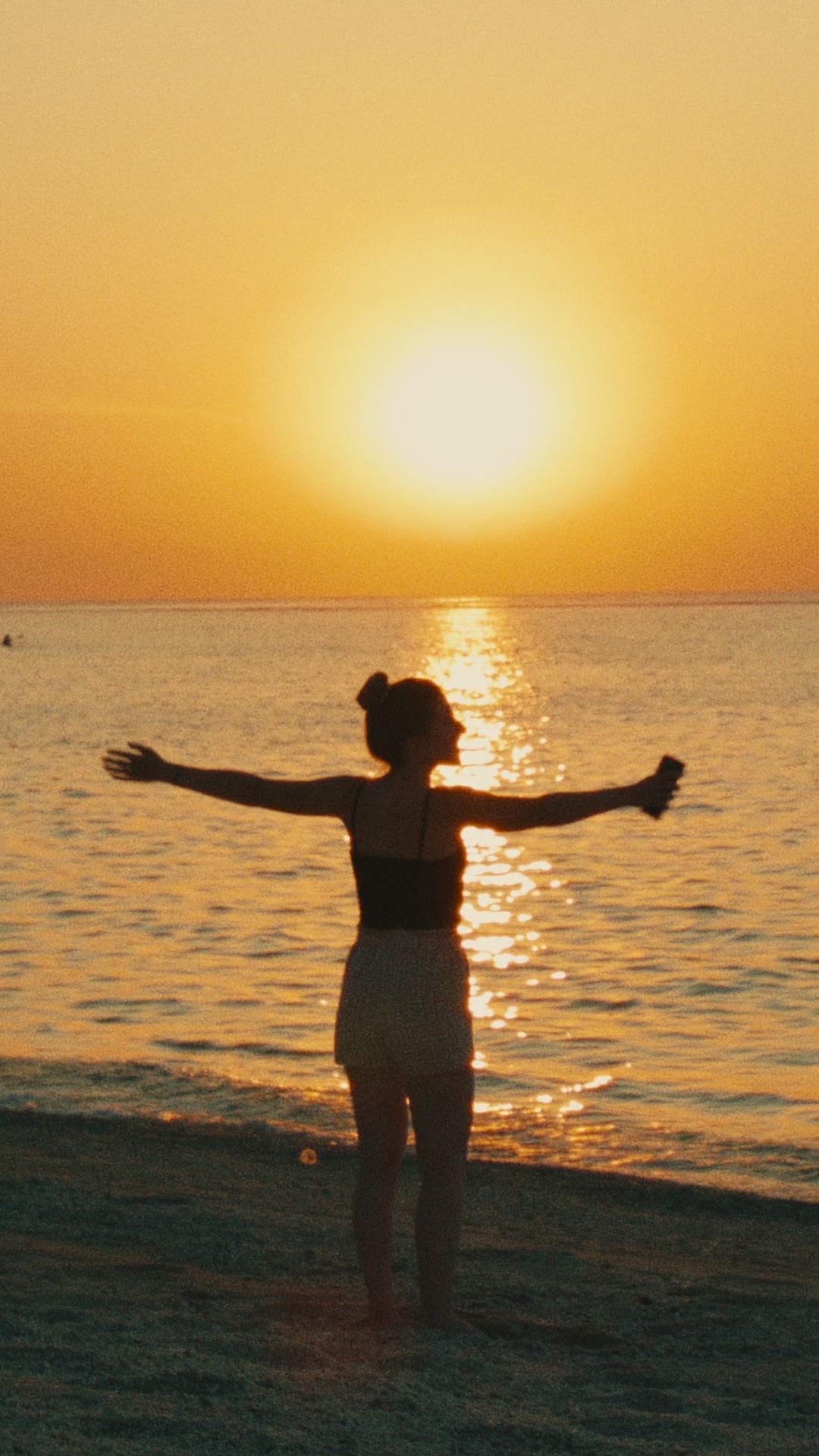 A woman standing by the sea in warm sunset light