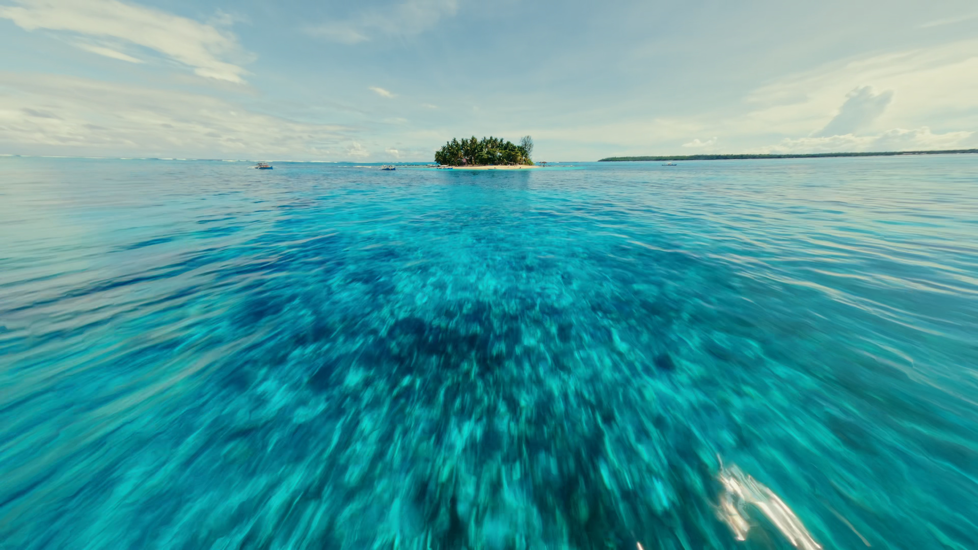 A low flight over clear water towards a small palm-covered island.